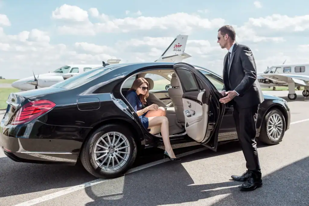 Elegant woman stepping out of a luxury car as a chauffeur holds the door, showcasing Bangkok luxury airport transfers.