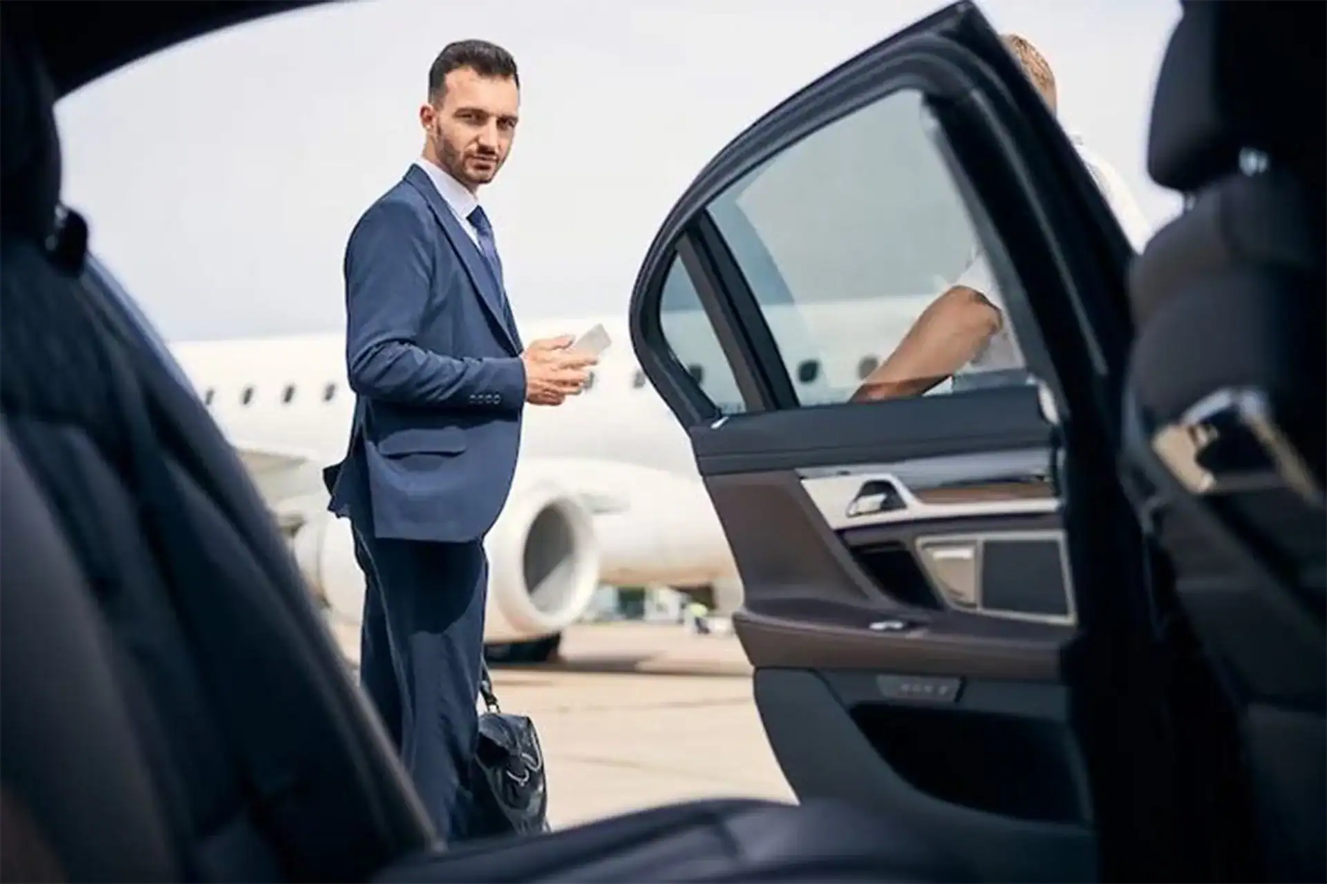 Business traveler in suit standing on airport runway holding a coffee cup, representing Bangkok luxury airport transfers.